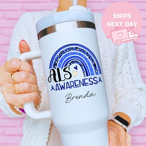 May include: White tumbler with a handle, featuring a blue and leopard print rainbow design. The text reads "ALS Awareness" and "Brenda". The tumbler has a white lid and a straw.