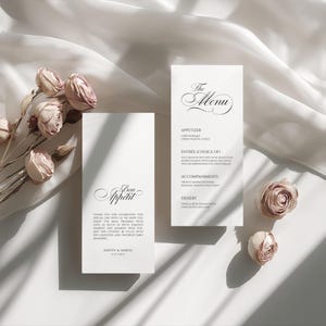 May include: Elegant wedding menu cards with floral accents. One card reads "The Menu" with a list of courses. The other card says "Bon Appétit" with a thank you message. Soft lighting and dried roses.