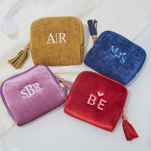 Peut inclure: Quatre petits porte-monnaie carrés en velours moutarde, bleu marine, violet et rouge. Chaque bourse a une fermeture éclair, un pompon et des initiales brodées. La bourse moutarde a "AR", la bourse marine a "M et S", la bourse violette a "SBR", et la bourse rouge a "BE".