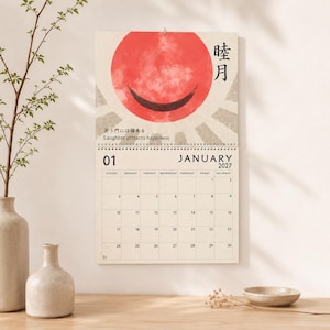 May include: A wall calendar for January 2027 featuring a red circular graphic with a black crescent shape, Japanese kanji characters, and the text Laughter attracts happiness. The grid displays dates from Sunday to Saturday in a clean layout.