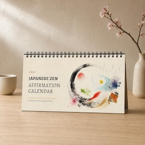 May include: A 2027 Japanese Zen Affirmation Calendar with a black spiral binding. The cover features the text "2027 JAPANESE ZEN AFFIRMATION CALENDAR" and "12 Japanese Proverbs for Mindful Growth" alongside a circular watercolour brushstroke design.