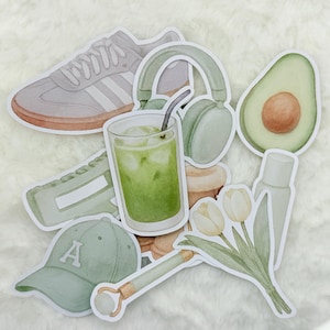 Peut inclure: Un ensemble d'autocollants verts et blancs représentant un casque audio, un verre de matcha glacé, une paire de baskets, un avocat vert, une casquette de baseball avec la lettre A, un rouleau de jade et un bouquet de tulipes blanches.