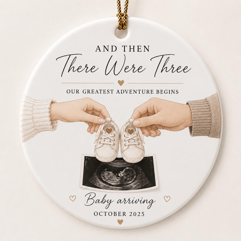 May include: Round white ceramic ornament with gold string, featuring the text "AND THEN There Were Three" and "OUR GREATEST ADVENTURE BEGINS". The ornament includes illustrations of baby shoes, an ultrasound image, and the text "Baby arriving OCTOBER 2025".
