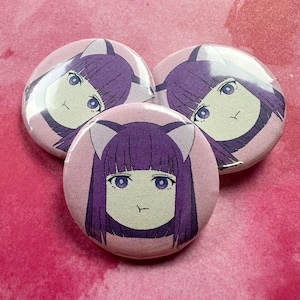 May include: Three round, pink buttons with a cartoon illustration of a girl with purple hair and cat ears. The girl has blue eyes and a neutral expression. The buttons are arranged on a pink background.
