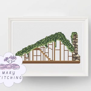 May include: Cross-stitch art of a building with a green vine-covered roof and a stone chimney. The building has a wooden frame and a staircase. The artwork is framed in a white frame. The logo for Mary Stitching is in the lower left corner.