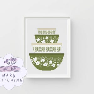 May include: A framed print showing a stack of four decorative mixing bowls. The bowls are olive green with white floral and geometric patterns. The lids are beige. The print is labeled "MARY STITCHING" in a floral design.