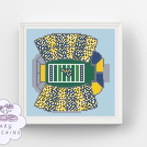 May include: A square cross-stitch pattern depicting an aerial view of a football stadium with a green field, yellow and blue seating sections, and a light blue background, framed in a white border. A logo with the text MARY STITCHING is visible.