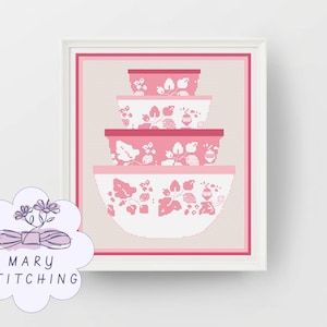 Op de afbeelding: Een ingelijst kruissteekkunstwerk met een stapel van vier roze en witte mengkommen. De kommen hebben een bloemenontwerp. Het kunstwerk is geplaatst tegen een neutrale achtergrond en omlijst in roze.