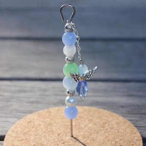 May include: A beaded angel ornament with a silver hook and chain. The ornament features a series of colorful beads in shades of blue, green, white, and pearl. A small silver angel charm with outstretched wings is attached.