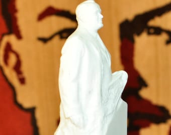 May include: White plaster bust of a man with a raised right hand, standing on a black base. The bust is inscribed with the text "АНДРЕЙ КОРОЛЕВ".