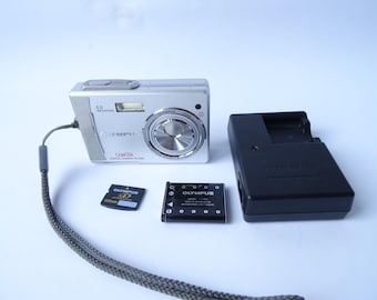 May include: Silver Olympus digital camera with a lens, flash, and strap. Includes a black battery charger, a black battery, and an Olympus XD memory card. The camera is labeled "CAMEDIA DIGITAL CAMERA C-460 ZOOM".