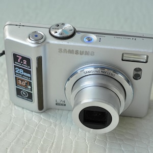 May include: A silver Samsung L74 digital camera with a 7.2 megapixel resolution, 28mm wide angle lens, and 3.0 inch touch screen LCD.