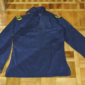 May include: A dark blue long-sleeved shirt with gold trim on the shoulders and red velvet on the cuffs.