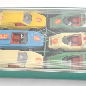 May include: A clear plastic case with six toy cars inside. The cars are yellow, blue, beige, green, and two are beige. Each car has a number "8" on the side and the word "AUTOCOR" is printed on the blue car.