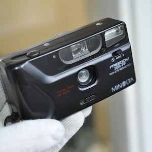 Könnte beinhalten: Eine schwarze Minolta Freedom 35R-FF Filmkamera mit einer Funktion zur Reduzierung von Rote-Augen-Effekten. Die Kamera verfügt über ein freies Fokus-Objektiv und einen Automatikmodus.
