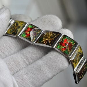 May include: A silver bracelet with square links, each decorated with a different floral design in red, green, yellow, and black enamel.