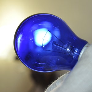 Può includere: Una lampadina blu con un filamento bianco all'interno. La lampadina è tenuta da una mano.