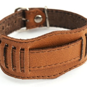 May include: A brown leather bracelet with a buckle closure and a decorative cut-out design.