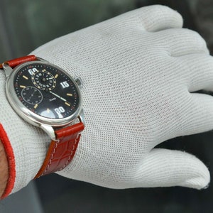 May include: A silver wristwatch with a black face and white numerals. The watch has a red leather band and a small second hand dial.