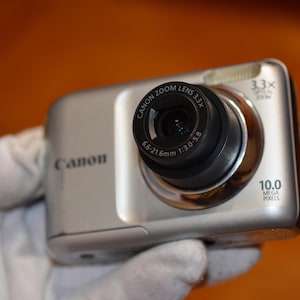 May include: A silver Canon digital camera with a 3.3x optical zoom lens and 10.0 megapixels. The lens has a 6.6-21.6mm focal length and a 1:3.0-5.8 aperture.