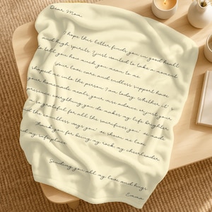 Puede incluir: Manta de color crema con escritura a mano en negro. El texto dice "Querida mamá" y un mensaje sincero que expresa amor y gratitud. Un regalo reflexivo para el Día de la Madre o cualquier ocasión.