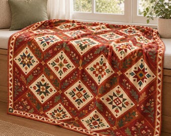 May include: A rectangular throw blanket featuring a repeating diamond pattern in shades of deep red, cream, green, and blue. The design includes geometric star motifs and floral elements within each diamond, finished with a triangular border.