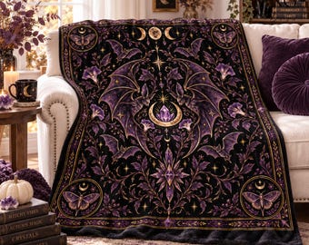 May include: A black throw blanket featuring a symmetrical design with purple and gold accents. The pattern includes winged creatures, crescent moons, stars, floral motifs, and a central crystal element. Four circular frames at the corners contain moth illustrations.
