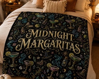 May include: A black throw blanket featuring the text Midnight Margaritas in gold lettering, surrounded by a repeating pattern of margarita glasses, witch hats, crystals, butterflies, and swirling smoke in shades of green, purple, and gold.