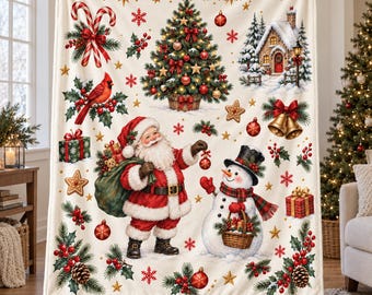 May include: A cream-colored throw blanket featuring a festive Christmas pattern with Santa Claus, a snowman, a decorated tree, a snowy cottage, candy canes, holly, and gift boxes. The design includes gold stars and red snowflakes throughout.
