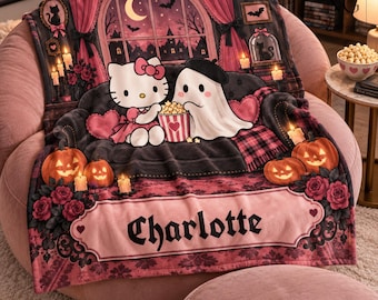 May include: A plush throw blanket featuring a graphic print of a white cat character and a ghost sitting on a dark sofa eating popcorn. The scene includes pumpkins, candles, roses, and a window with a crescent moon. The name Charlotte is printed below.