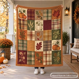Puede incluir: Una manta rectangular con un diseño de patchwork de cuadrados con temática otoñal. El patrón incluye ilustraciones de calabazas naranjas, bellotas, tallos de trigo y hojas de otoño coloridas, alternadas con varias texturas de tela a cuadros.