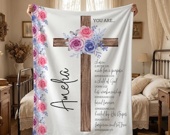 May include: White blanket with a wooden cross design, adorned with pink, purple, and blue floral accents. The blanket features the name "Amelia" and inspirational text. A decorative and comforting home decor item.