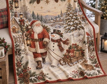 May include: A cream-colored throw blanket featuring a festive winter scene with Santa Claus holding a lantern, a snowman pulling a wooden sled filled with wrapped gifts, a decorated Christmas tree, pine branches, and a rabbit.