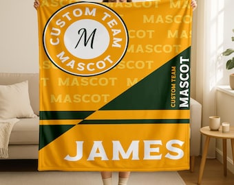May include: A yellow and green blanket with the text "CUSTOM TEAM MASCOT" in a circle, and the name "JAMES" in large white letters. The blanket has a diagonal green stripe and horizontal green stripes.