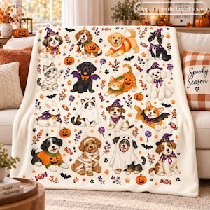 May include: A cream-colored fleece blanket featuring a repeating pattern of puppies and kittens dressed in Halloween costumes, including pumpkins, ghosts, and witch hats, interspersed with small bats, paw prints, and colorful candy illustrations.