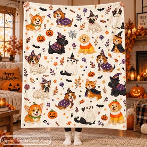 May include: A cream-colored fleece blanket featuring a repeating pattern of puppies and kittens dressed in Halloween costumes, including witch hats, capes, and ghost sheets, interspersed with orange pumpkins, bats, and colorful candy icons.