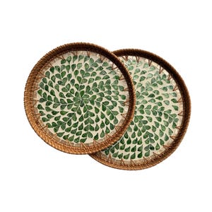 以下が含まれることがあります： 茶色の縁と、緑の葉の形模様で装飾された白い内装の、2つの丸い織りトレイ。 トレイは天然素材で作られており、食品の提供に適しています。