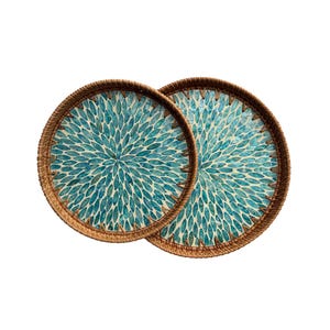 May include: Two round decorative trays with a woven brown border. The tray's interior features a pattern of teal-colored leaf shapes against a cream background. These trays are ideal for serving or display.