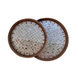 Könnte beinhalten: Zwei runde Untersetzer mit einem gewebten braunen Rand. Die Mitte jedes Untersetzers weist ein schuppenartiges Muster in Weiß- und Beigetönen auf. Die Untersetzer dienen dazu, Oberflächen vor Kondenswasser von Getränken zu schützen.
