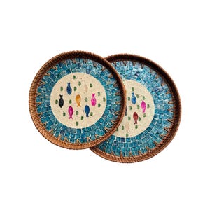 Puede incluir: Dos bandejas redondas decorativas con diseño de mosaico. El borde exterior es marrón tejido, y el centro presenta un mosaico azul claro con ilustraciones de peces coloridos. Los peces son en tonos negro, amarillo, rosa y azul.