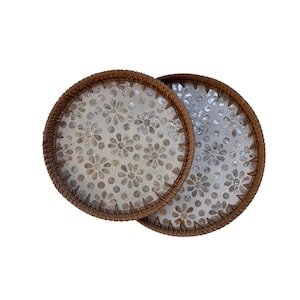 Puede incluir: Dos posavasos redondos con un borde tejido marrón y un estampado floral. Los posavasos tienen un diseño floral de color claro en el interior. Están hechos de materiales naturales y son adecuados para la decoración del hogar.