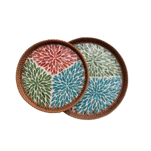 May include: Two round coasters with a woven brown border. Each coaster features a floral design in quadrants of red, green, blue, and white. These decorative coasters are perfect for protecting surfaces from drink rings.
