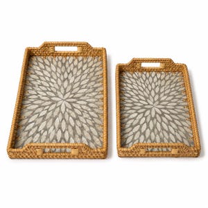 May include: Two rectangular serving trays with woven light brown rattan frames and integrated handles. The base of each tray features a grey and white floral-inspired petal pattern arranged in a radiating sunburst design across the flat surface.