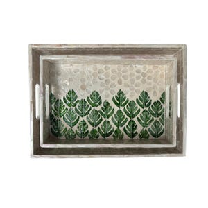 May include: Two rectangular decorative trays. The trays are nested, with a larger tray and a smaller tray inside. The interior of the trays features a pattern of green leaves and a pebble design. The trays have a light-colored, textured border and cut-out handles.