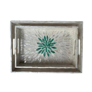May include: Two rectangular serving trays nested together. The trays have a light grey wooden frame and a mother-of-pearl inlay. A green floral design is in the centre of the trays. Each tray has two handles.