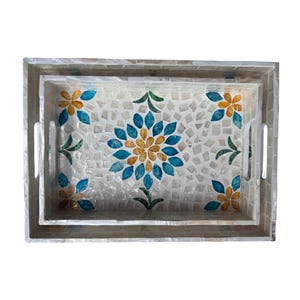 May include: A pair of rectangular serving trays with a mosaic design. The trays have a central floral pattern in blue and gold, set against white tiles. They feature handles and a light-coloured border. The trays are ideal for serving.