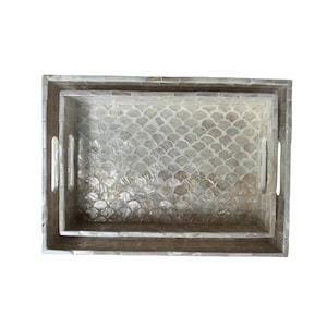 May include: Two rectangular decorative trays. The larger tray has a smaller tray nested inside. Both trays are light gray with a mother-of-pearl finish and a scale-like pattern. Each tray has two handles.