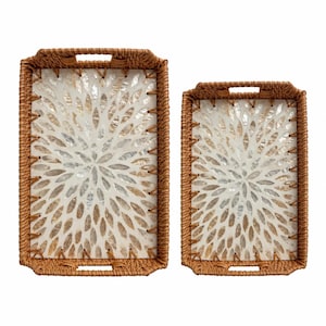 May include: Two rectangular serving trays with woven brown rattan frames and integrated handles. The base of each tray features a white, petal-like floral cutout overlay set against a shimmering, iridescent mother-of-pearl shell inlay.