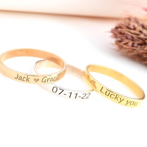 Puede incluir: Tres anillos dorados y plateados con texto grabado. Uno dice "Jack ♥ Gracie", otro "07-11-22" y el tercero "Lucky you". Los anillos se muestran sobre una superficie blanca.