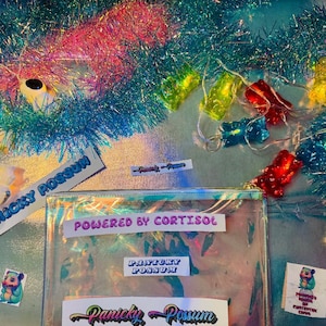 May include: A clear, iridescent pouch with the text "POWERED BY CORTISOL" and "PANICKY POSSUM". The image includes colorful gummy bear lights, a sticker with a cartoon possum, and a banner that says "PANICKY POSSUM".